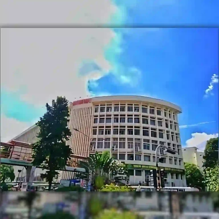 Modern multi-story building with curved facade under blue sky with clouds.