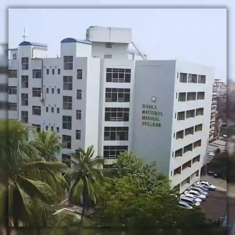 Modern multi-story building with large windows and surrounding greenery against an overcast sky.