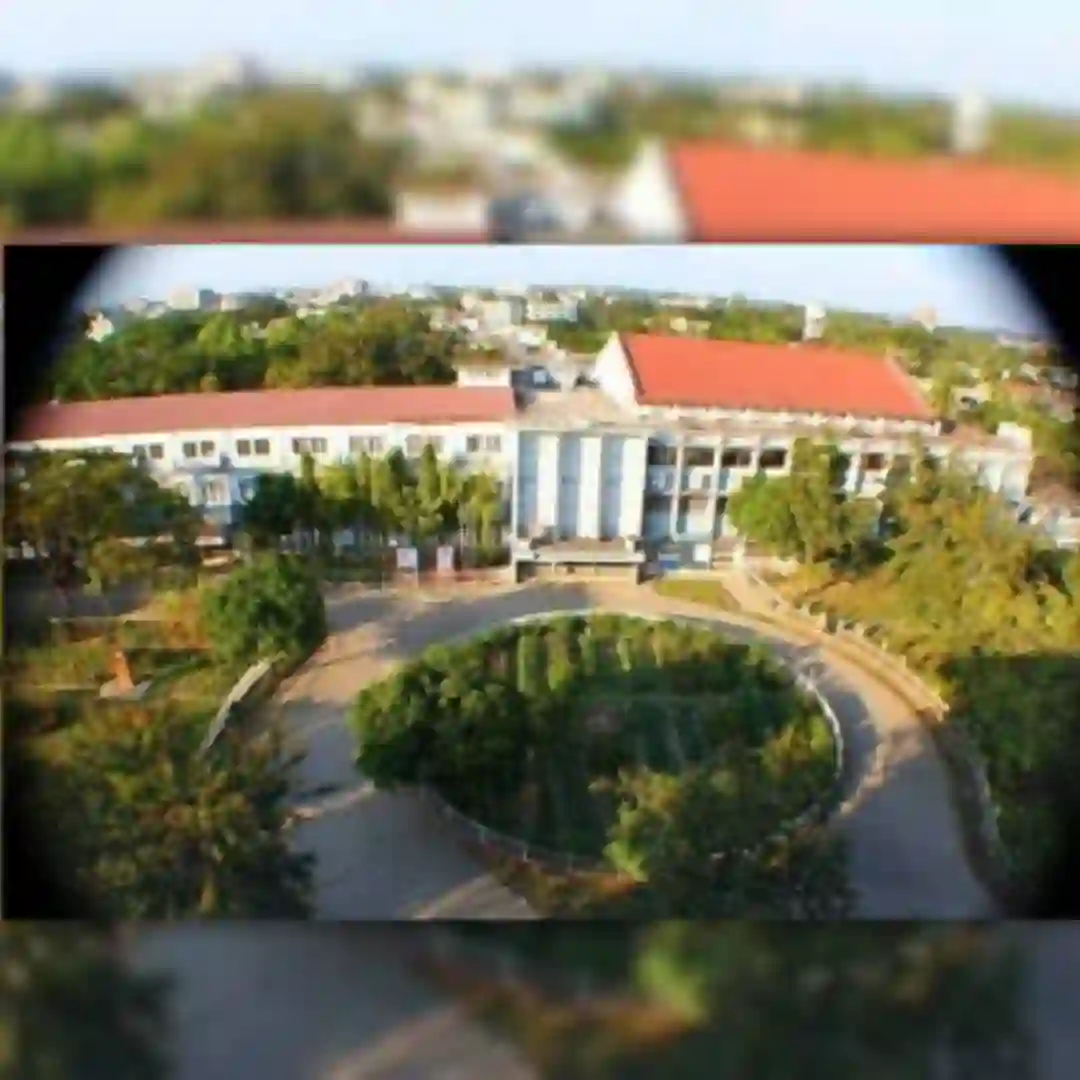 Aerial view of a building with a red roof surrounded by greenery, with image edges blurred.