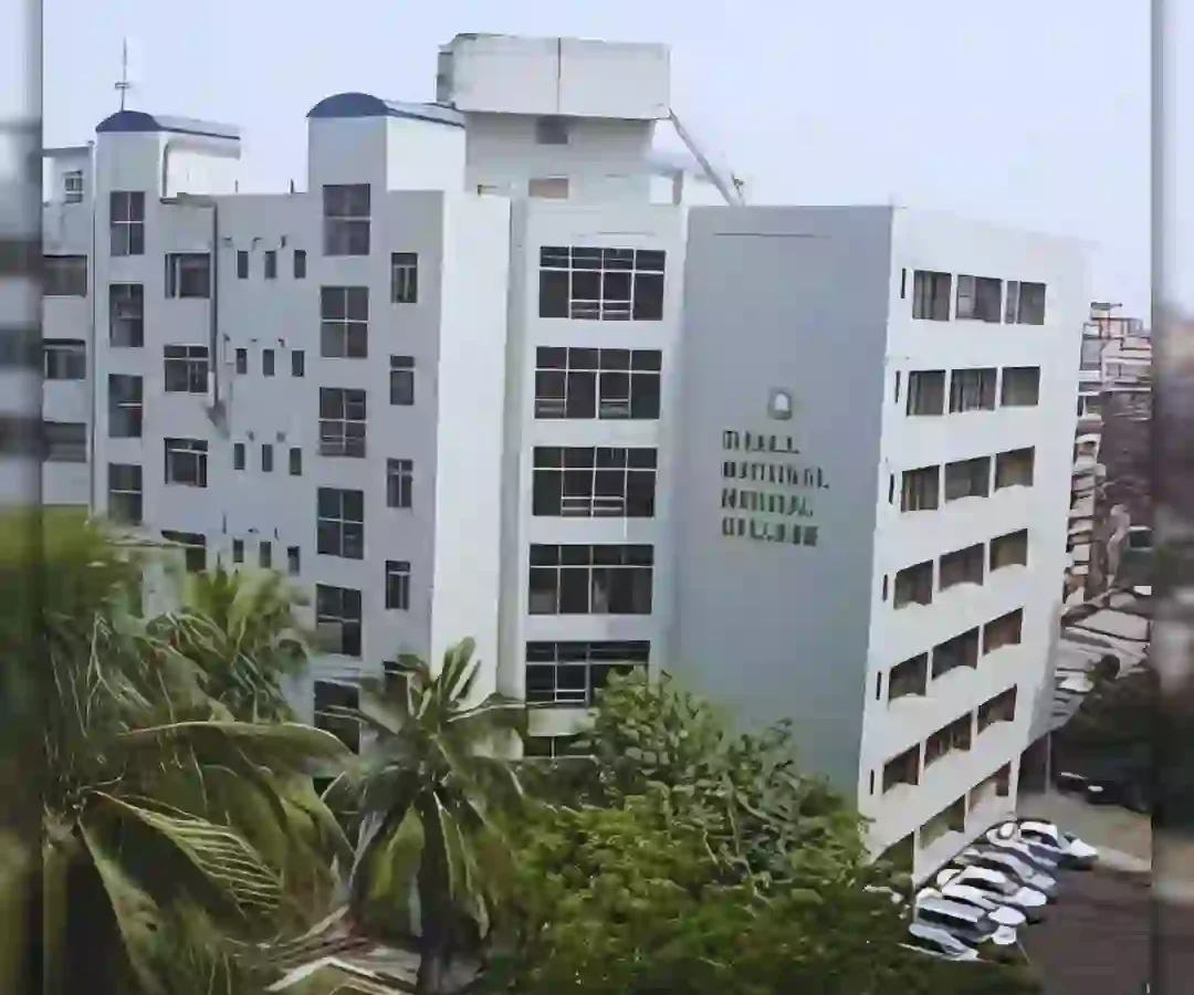 Modern multi-story building with large windows and surrounding greenery against an overcast sky.