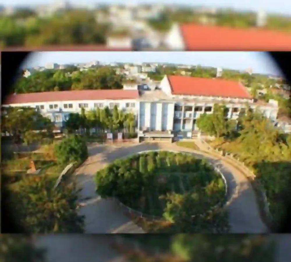 Aerial view of a building with a red roof surrounded by greenery, with image edges blurred.